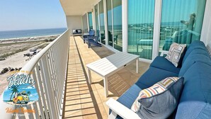 A balcony with a view of the beach and ocean. There is a white table and blue sofa with pillows. - Flash Sale. Caribe D1108. Sleeps 10 (Orange Beach)