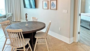 A hotel room with a bed, a dining area with a table and chairs, a ceiling fan, and framed artwork on the wall. - Flash Sale. Caribe D1108. Sleeps 10 (Orange Beach)