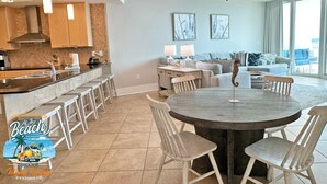 A modern kitchen with a bar area, a dining table with chairs, and a living area with a sofa and a seahorse decoration. - Flash Sale. Caribe D1108. Sleeps 10 (Orange Beach)