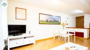 A living room with a flat-screen TV, a white entertainment unit, a dining table with chairs, and a painting on the wall. - Mezzanine 26 by TuscanyWeGo (Lucca)