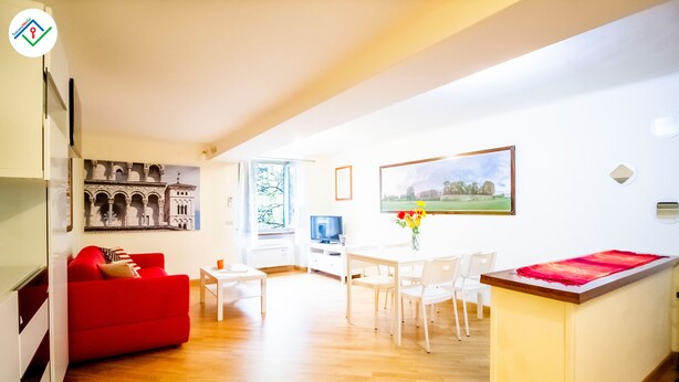 A modern living room with a red sofa, a dining area with a white table and chairs, and a kitchen island. - Mezzanine 26 by TuscanyWeGo (Lucca)