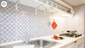 A kitchen with a stainless steel sink, white countertop, patterned backsplash, and a red hanging pot holder. - Mezzanine 26 by TuscanyWeGo (Lucca)