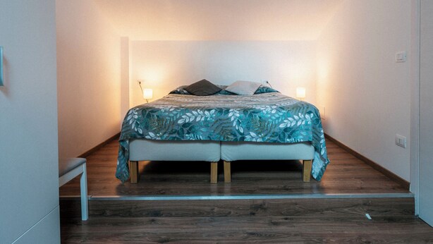 A bedroom with a bed, wooden floor, and two bedside lamps. - Guest House All'83 (Grosseto)