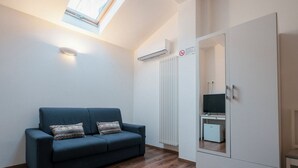 A room with a dark blue sofa, a white wardrobe, a radiator, and a skylight. - Guest House All'83 (Grosseto)