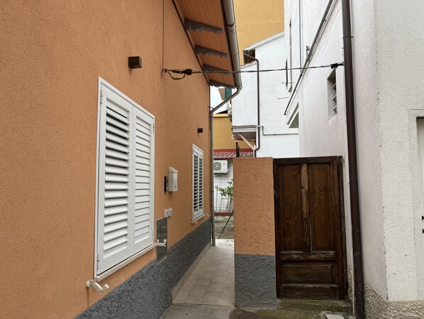 A narrow alleyway with a white door on the right and a white window with shutters on the left.