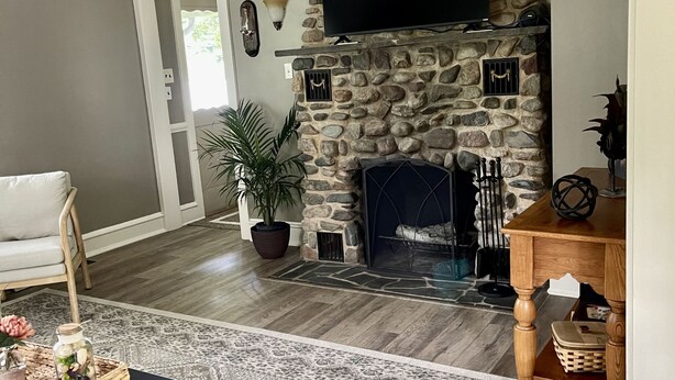 A living room with a stone fireplace, a flat-screen TV mounted above it, a ceiling fan, and a patterned rug. - Quiet secluded home~ minutes from Ocean City boardwalk and beaches (Egg Harbor Township)