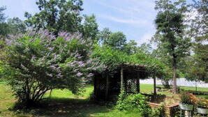 A garden with a pergola, lush greenery, and a body of water in the background. - Quiet secluded home~ minutes from Ocean City boardwalk and beaches (Egg Harbor Township)