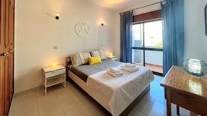 Ein Schlafzimmer mit Bett, Nachttischen, einem Fenster mit Vorhängen und Blick ins Freie.