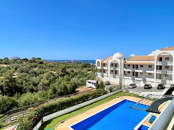 A resort with a swimming pool, a view of the sea, and a white building with balconies.