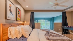 Een slaapkamer met een groot bed, een houten hoofdbord, een plafondventilator en uitzicht op een balkon.
