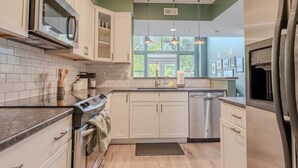 Een moderne keuken met witte kasten, roestvrijstalen apparatuur en een groot raam dat zorgt voor natuurlijk licht.