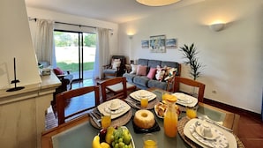 Un comedor con una mesa dispuesta para el desayuno, un sofá al fondo y vistas al exterior.