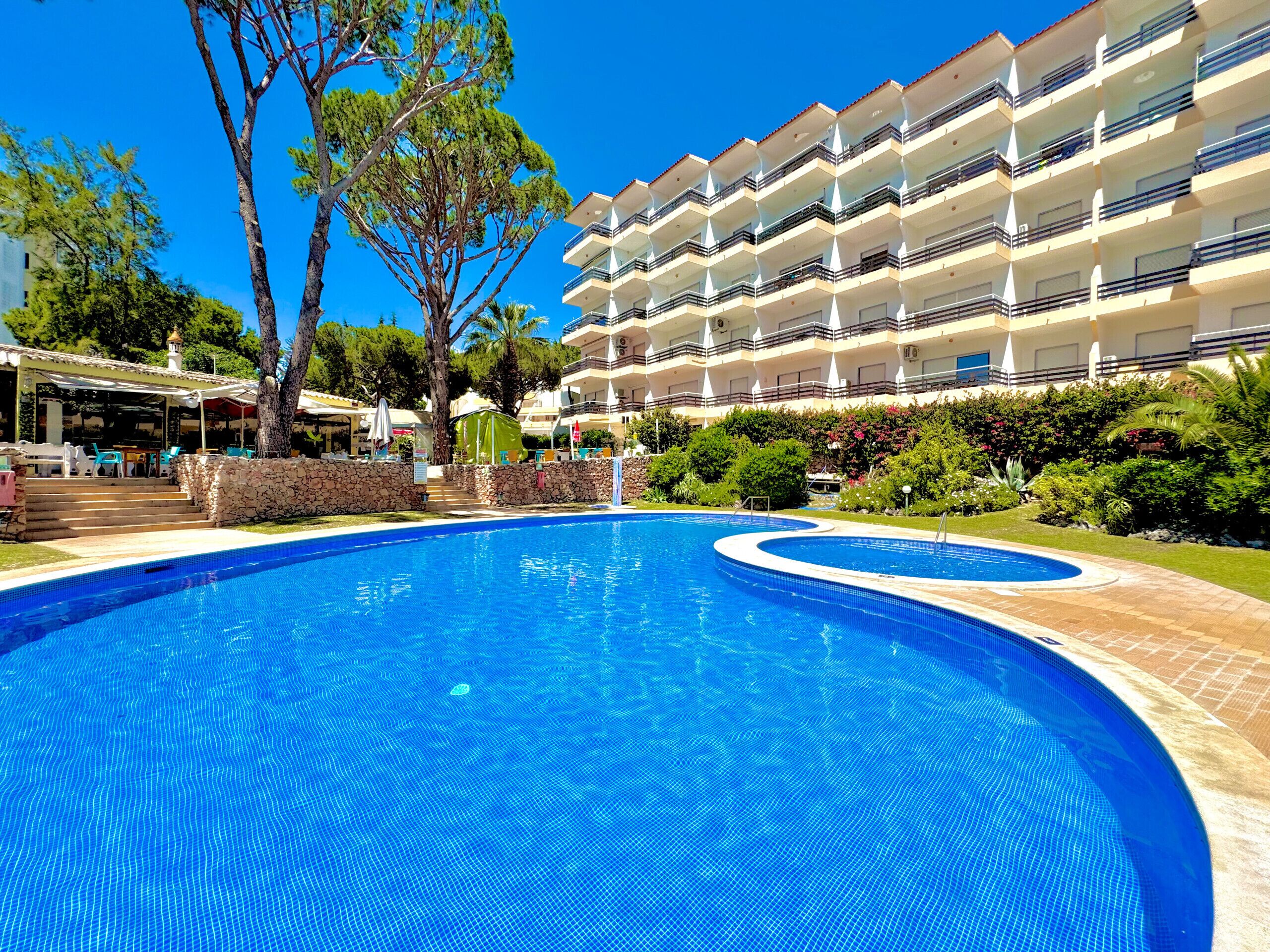 Una piscina con bordura in pietra, circondata da un giardino curato e un edificio a più piani con balconi.