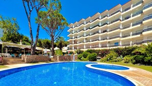 Une piscine bordée de pierres, entourée d’un jardin bien entretenu et d’un immeuble à plusieurs étages doté de balcons.