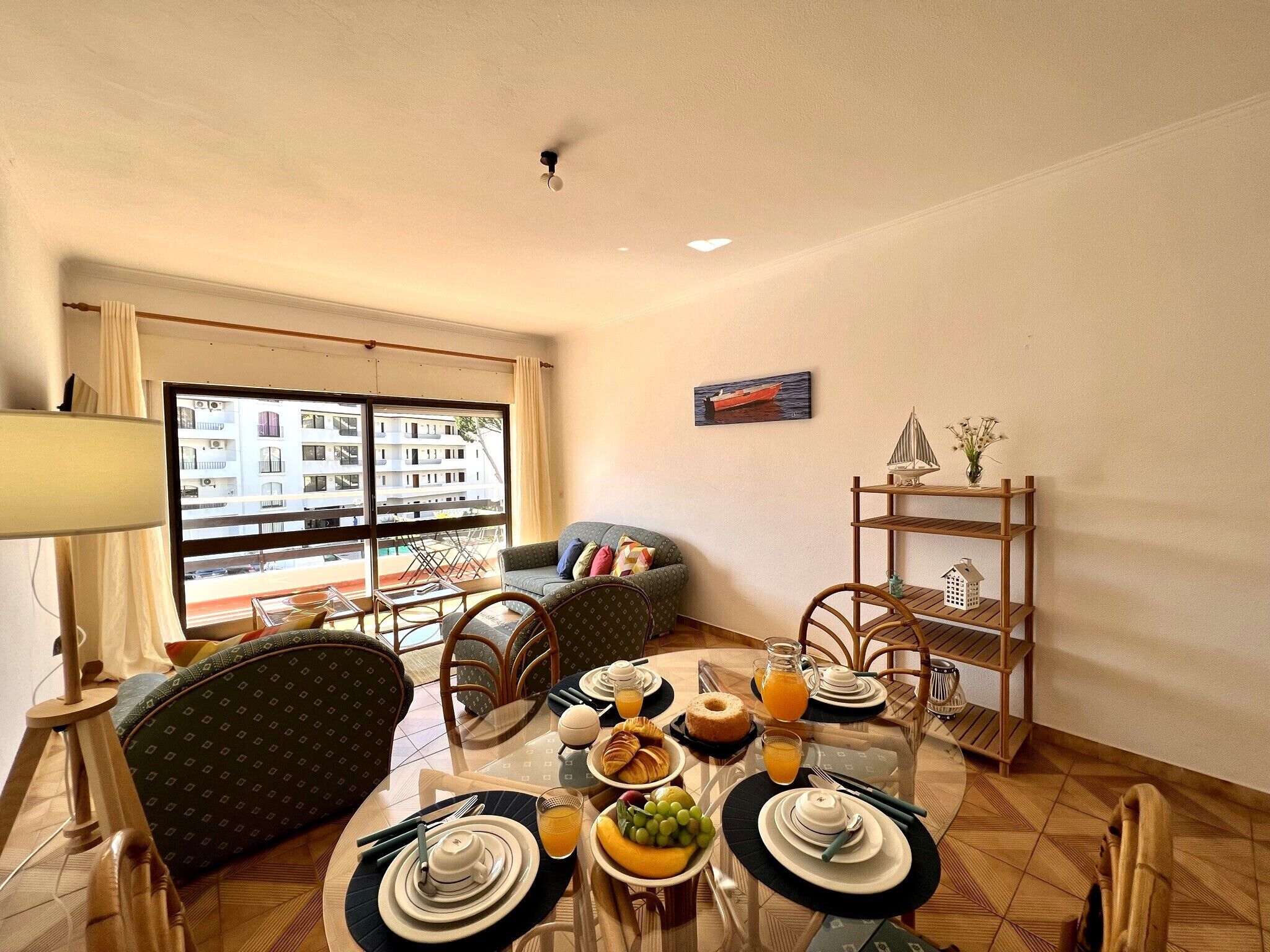 Zona pranzo con tavolo apparecchiato per la colazione, sedie, divano e vista su un edificio attraverso ampie finestre.