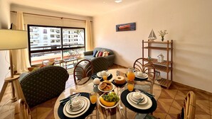 Un coin repas avec une table mise pour le petit-déjeuner, des chaises, un canapé et une vue sur un immeuble à travers de grandes fenêtres.