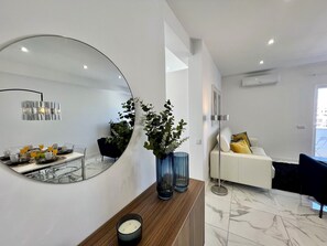 A modern living room with a large mirror, a wooden console table, a floor lamp, and a white sofa with yellow cushions.