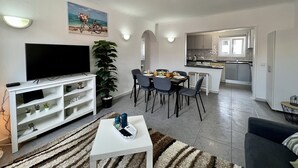 Ett modernt vardagsrum med en platt-TV, ett soffbord och en matplats med stolar och ett bord.
