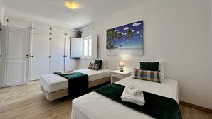 Ett hotellrum med två sängar, en garderob, en tavla som föreställer en strandscen och en taklampa.