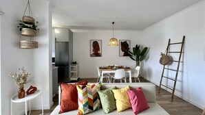 A modern living room with a sofa, colorful cushions, a dining area with a table and chairs, a kitchen in the background, and decorative baskets and plants. - ALBUFEIRA DESIGN by HOMING (Albufeira)