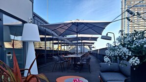 An outdoor seating area with tables and chairs, umbrellas, and a sofa. - ASTON HOTEL RIGA (Riga)