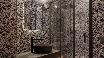 A modern bathroom with a black stone sink, a glass shower enclosure, and a terrazzo floor.