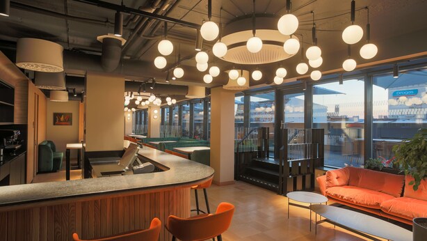 A modern interior with a bar area, seating, and large windows offering a view of the city. - ASTON HOTEL RIGA (Riga)