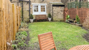 A stone house with a wooden fence, a bench, and a small garden. - Cherry Tree Cottage (Bingley)
