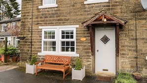 A stone house with a white door, a wooden bench, and a small garden. - Cherry Tree Cottage (Bingley)
