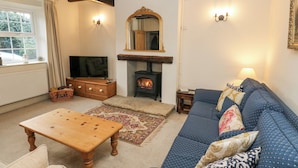 A cozy living room with a fireplace, a sofa, a wooden coffee table, and a television. - Cherry Tree Cottage (Bingley)