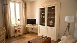 Un salon avec un plancher en bois, un canapé blanc, un meuble en bois doté de portes en verre, un téléviseur posé sur un bureau en bois et une lampe.