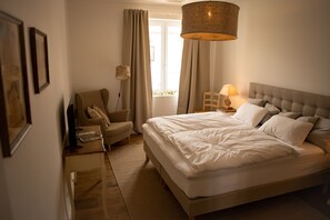 Une chambre à coucher avec un grand lit, une chaise, une table de chevet et une fenêtre avec des rideaux.