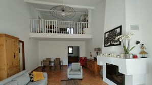 A spacious living area with a high ceiling, a fireplace, and a dining area with chairs and a sofa. - Bienvenue Dans Notre Villa Provençale (Fréjus)