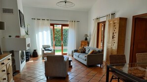 A spacious living area with a sofa, armchairs, and a dining table. There is a sliding glass door leading to a garden. - Bienvenue Dans Notre Villa Provençale (Fréjus)