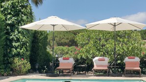 A poolside area with lounge chairs and umbrellas, surrounded by lush greenery. - Bienvenue Dans Notre Villa Provençale (Fréjus)