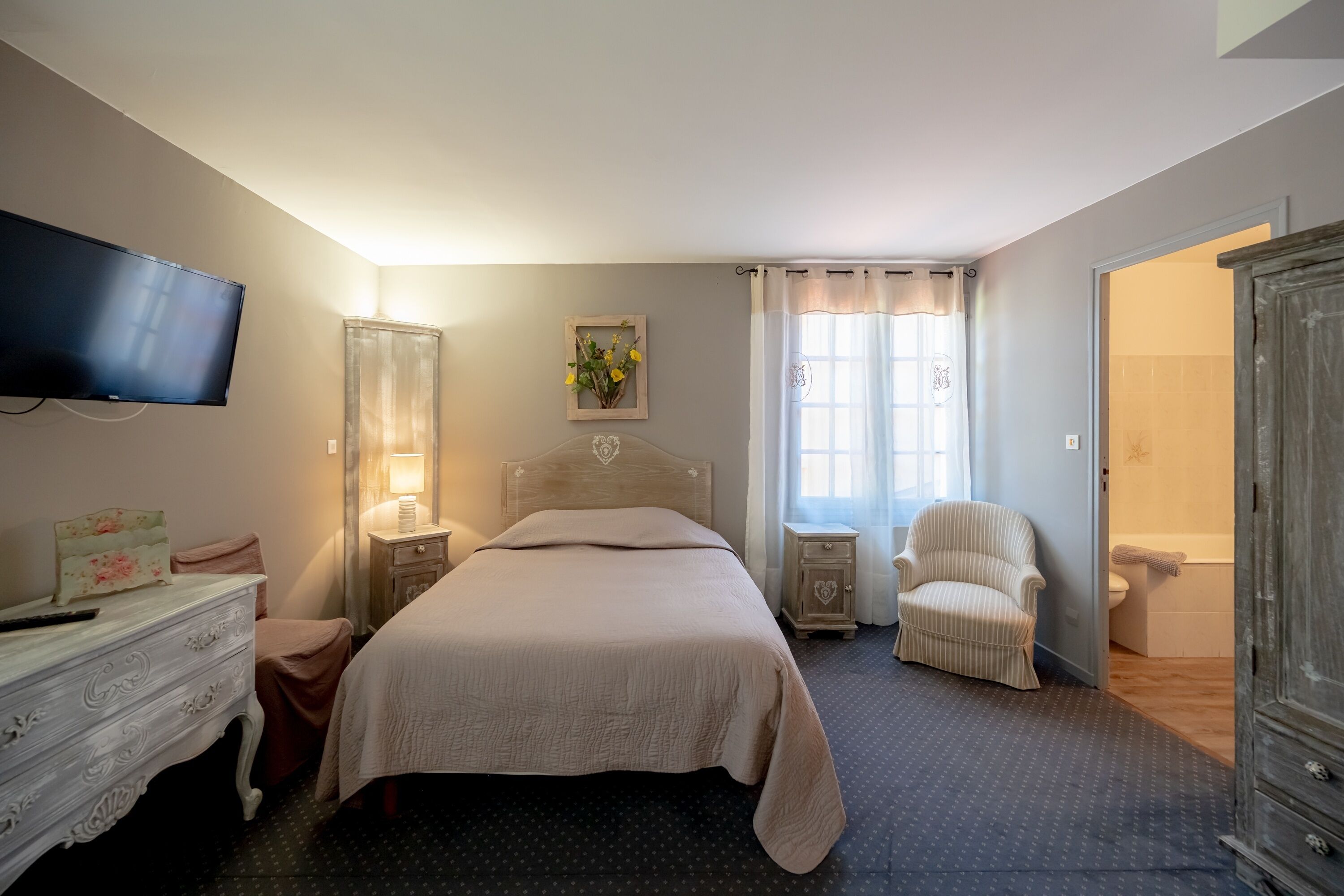 A bedroom with a bed, bedside table, lamp, chair, and a television mounted on the wall.