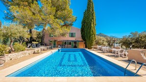 A swimming pool with a clear blue water pattern, surrounded by outdoor seating and a building with a tiled roof.