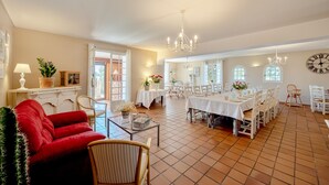 A spacious dining area with multiple tables and chairs, a red sofa, and a chandelier.