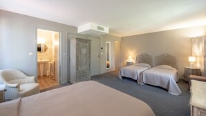 A hotel room with a large bed, two smaller beds, a chair, a wardrobe, and a bathroom visible through an open door.