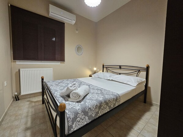 A bedroom with a bed, a radiator, an air conditioner, a window with a blind, and a wall-mounted light.