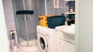 Ett litet badrum med tvättmaskin, en duschkabin med glasväggar och ett handfat.