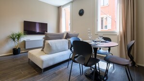A modern living room with a sofa, a TV, a dining table with chairs, and a potted plant. - Golden Suite by Studio Vita (Bologna)