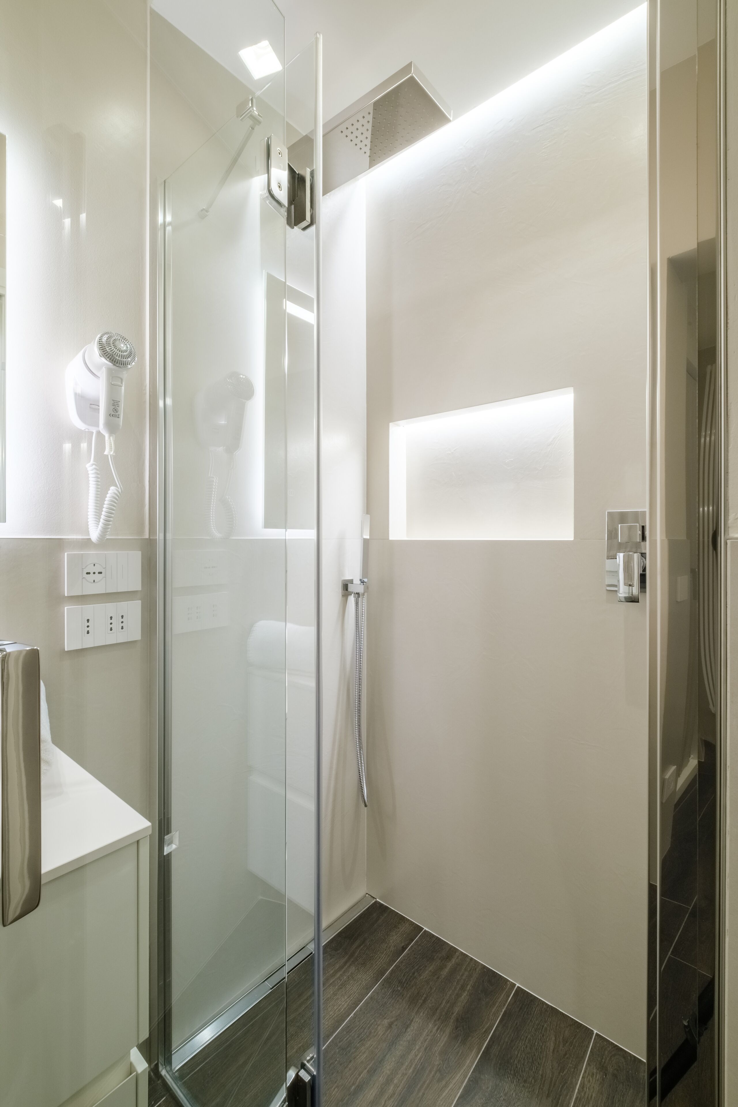 A modern bathroom with a glass shower enclosure, a hairdryer, and a towel rack.