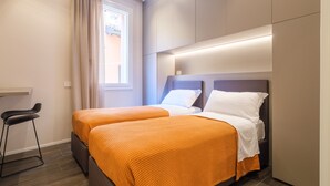 A hotel room with two beds, a small stool, a window with curtains, and a built-in headboard with integrated lighting. - Golden Suite by Studio Vita (Bologna)