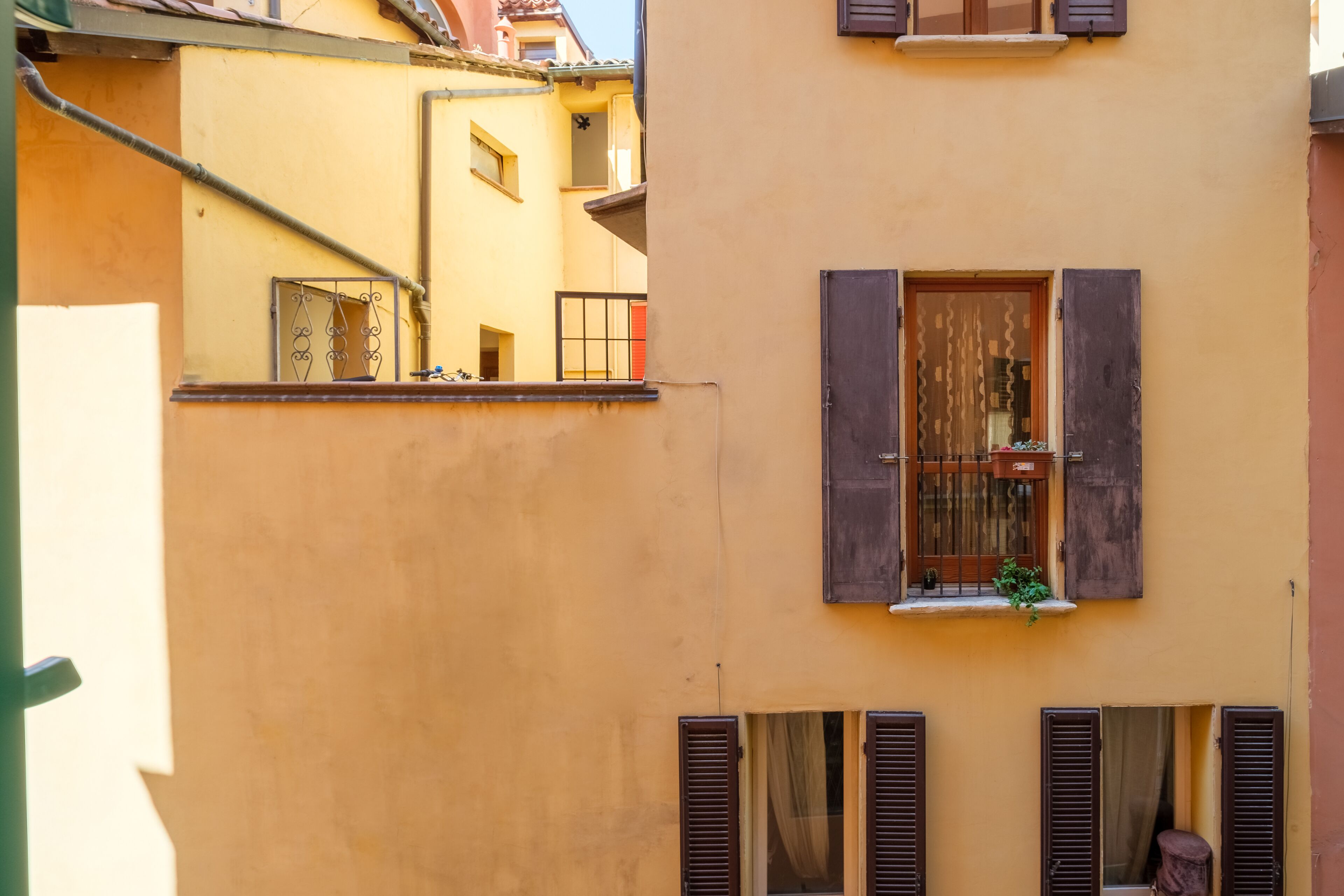 A building with a yellow facade, wooden shutters, and a small balcony with a plant.