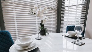 A dining table with white plates, a vase with white flowers, and two wine glasses. - Luxury Apartment close to the Beach (Llandudno)