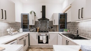 A modern kitchen with white cabinets, a black range hood, a built-in oven, and a stainless steel sink. - Luxury Apartment close to the Beach (Llandudno)