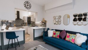 A modern kitchen with a central island, a dining area with a blue sofa, and decorative wall mirrors. - Luxury Apartment close to the Beach (Llandudno)