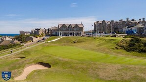 A golf course with a clubhouse, a sandy bunker, and a coastal backdrop.