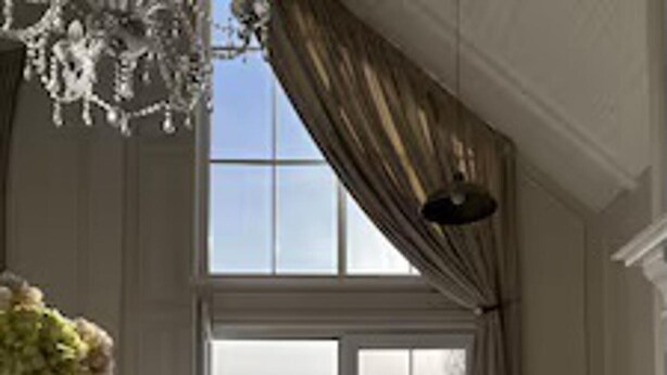 A spacious room with a large window, a chandelier, and a white dresser.